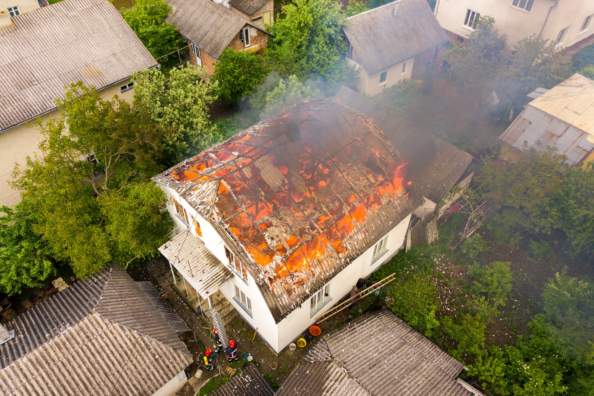 Aerial view of a house on fire with orange flames and white thick smoke