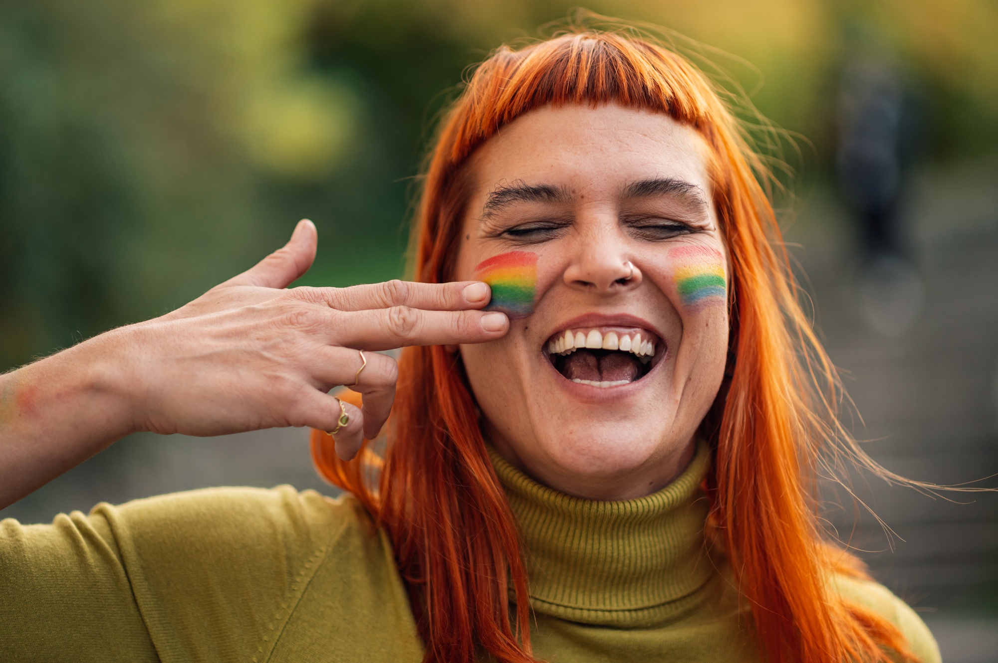 Woman with rainbow flag on her face is pointing at it and laughing